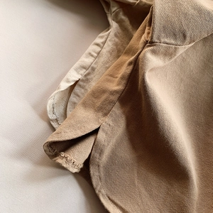 Macro view of khaki twill cotton shirt hem featuring split sides and precision stitching