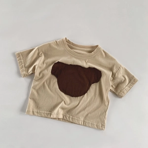 Détail d'un t-shirt enfant en coton avec un patch ours mignon sur tissu beige doux