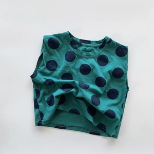 Flat lay macro view of a green kids tank top with large black polka dots and soft texture