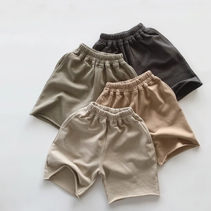 Flat lay of four children's cotton shorts in earth tones with elastic waist and raw edges