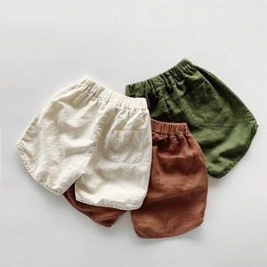Flat lay of three children's linen shorts in cream, olive, and brown with elastic waist