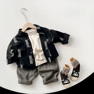Mise à plat d'une chemise enfant noire, d'un t-shirt blanc et d'un pantalon gris de style coréen