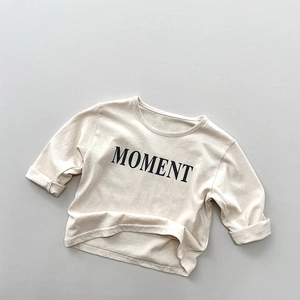 Detailaufnahme des MOMENT Buchstabendrucks und der Baumwolltextur des beigen Kinder-T-Shirts