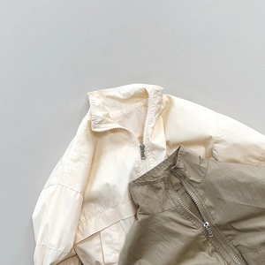 Dettaglio di giacche a vento per bambini in beige e oliva con cerniera a collo alto