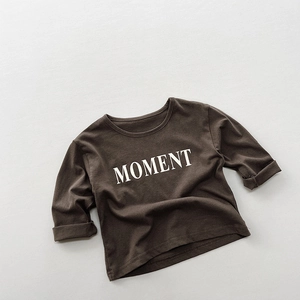 Detailaufnahme von weichem Baumwollstoff und MOMENT-Buchstabendruck auf braunem Kinder-T-Shirt
