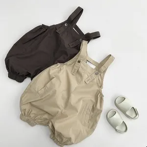 Flat lay detail of cotton baby overalls in dark brown and beige with adjustable buckles
