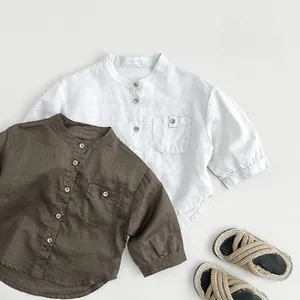 Flat lay of white and olive cotton linen kids shirts with wooden buttons and straw sandals