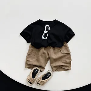 Flat lay of kids black cotton T-shirt with brown cargo shorts and straw sandals set