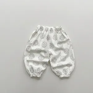Close-up of lightweight white cotton kids pants with black leaf print and elastic cuffs