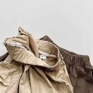 Detail of elastic waistbands and pockets on khaki and brown cotton cargo shorts for kids