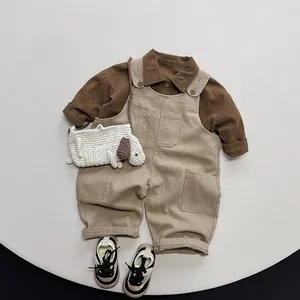 Mise à plat d'un ensemble bébé d'automne avec chemise marron et salopette kaki sur fond blanc