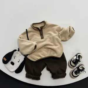 Flat lay of beige fleece pullover and dark brown pants set on a minimalist white platform