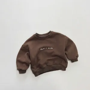Close-up of brown kid's fleece sweatshirt featuring Dad < mom print and ribbed cuffs