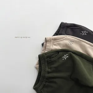 Détail de trois joggings pour enfants doublés en polaire en gris, beige et vert brodés
