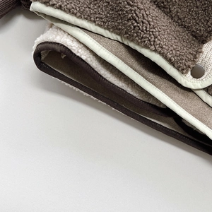 Close-up of thick brown sherpa fleece fabric with cream piping and a metal snap button