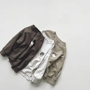 Flat lay detail of earth-tone children's cotton long sleeve shirts with small bear prints
