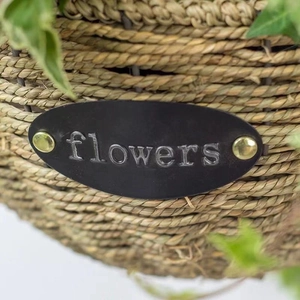 Hanging woven plant basket with flowers metal plate and green decorative leaves