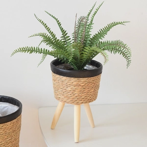 Close-up of handwoven wicker plant stand with black leather trim and wooden legs