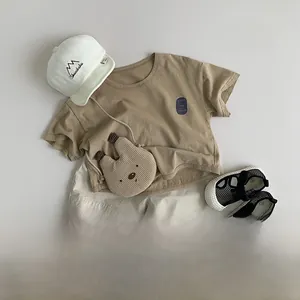 Flat lay of kids summer outfit with brown t-shirt, beige shorts and a cute bear bag