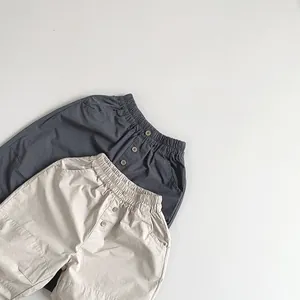 Detail view of kids loose cotton pants with elastic waist and button accents in grey and beige