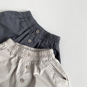 Detail of kids casual cotton linen pants showing elastic waist and decorative buttons