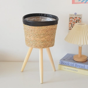Detail of hand-woven wicker plant stand with black leather rim and natural wooden legs