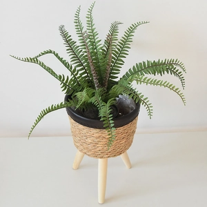 Close-up of woven straw plant pot with wooden legs and artificial Boston fern decoration