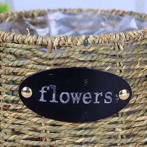 Detail of hand-woven straw basket featuring a metal flowers tag and waterproof plastic lining
