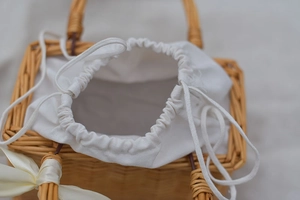 Detail of hand-woven wicker bag with white drawstring lining and a silk ribbon bow