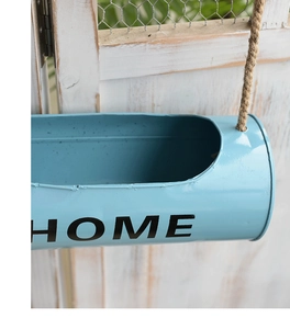 Detail of light blue metal hanging pot with jute rope and HOME text on wood fence