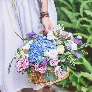 Oval wicker basket with blue hydrangeas and pink roses held by a girl in white dress
