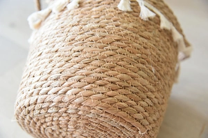 Close-up of natural wicker weave and white cotton tassel detail on bohemian flower basket