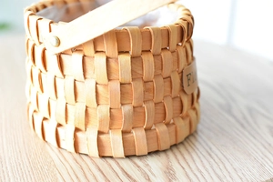Close-up of a woven wooden gift basket with a decorative leather flower tag and handle