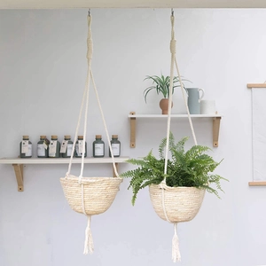 Detail of hand-woven hanging basket with tassels and green ferns on a white wall