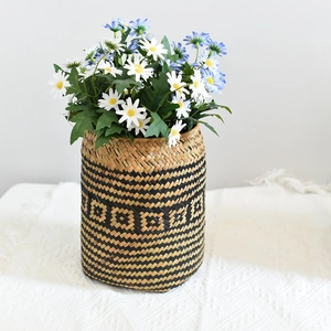 Detail of hand-woven seagrass basket featuring black geometric patterns and fresh daisies