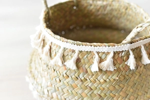 Detail of woven straw basket featuring white cotton tassels and natural fiber texture