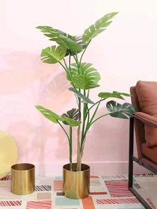 Detailed view of artificial Monstera plant in a modern golden metal cylinder flower pot