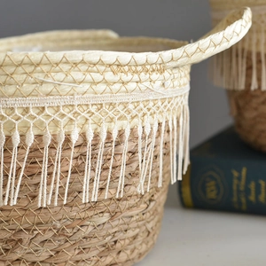 Handwoven seagrass plant basket with white tassels and handles in a cozy home setting
