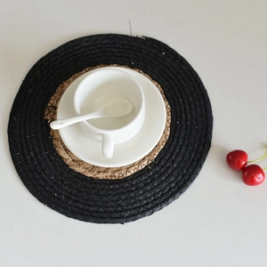 Top view of a round woven seagrass placemat with a black border and natural straw center