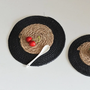 Close-up of circular woven seagrass heat-resistant coaster with natural and black spiral pattern