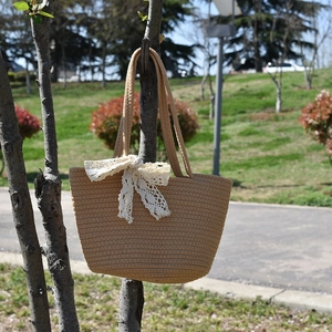 Close-up of beige woven tote bag with white lace bow detail hanging on a tree branch