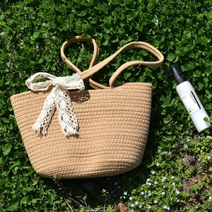 Detail of woven straw bag with white lace bow on fresh green grass background