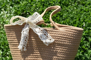 Close-up of woven straw handbag featuring a delicate white lace bow on natural green grass