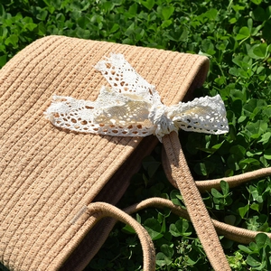 Detail shot of handwoven straw handbag texture with a large white lace bow on green grass