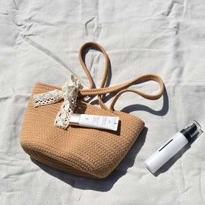 Close-up of a brown woven tote bag with white lace ribbon on a floral picnic mat