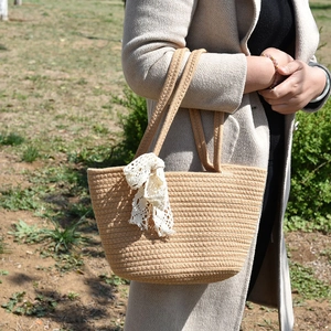 Detail of woven straw bucket bag featuring a cream lace bow and circular handles