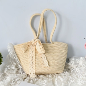 Detail of beige straw tote bag with lace bow and long strap on a vintage lace surface