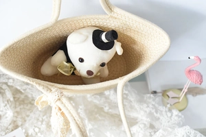 Detail view of woven cotton straw handbag with a plush bear inside on lace tablecloth