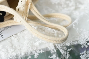 Close-up of woven rope handle and white floral lace detail on the beige hand-woven bag