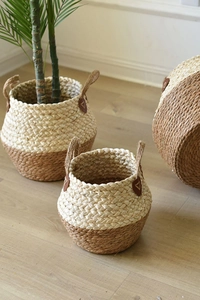 Close-up of three woven seagrass planters with leather accents and rope handles on wood floor